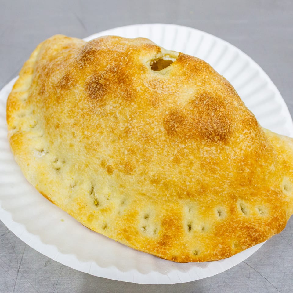 Golden-brown baked bread with a crisp, textured crust sits on a white paper plate.