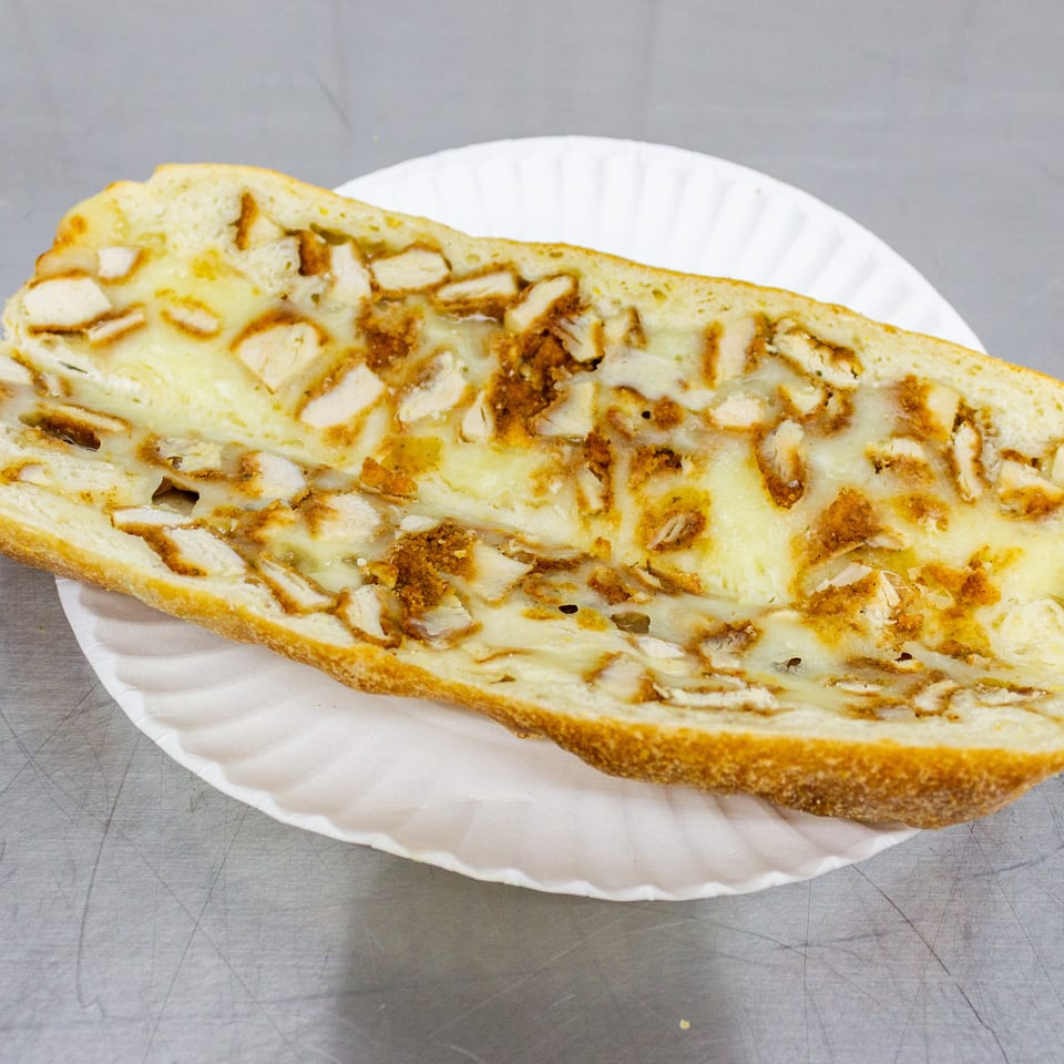 Toasted chicken and melted cheese sandwich served open-faced on a white paper plate.
