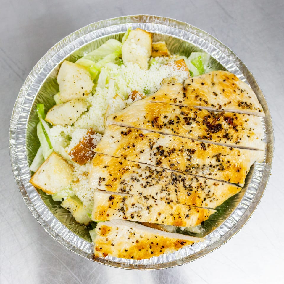 Grilled chicken Caesar salad with romaine lettuce, croutons, and Parmesan in a foil tray.