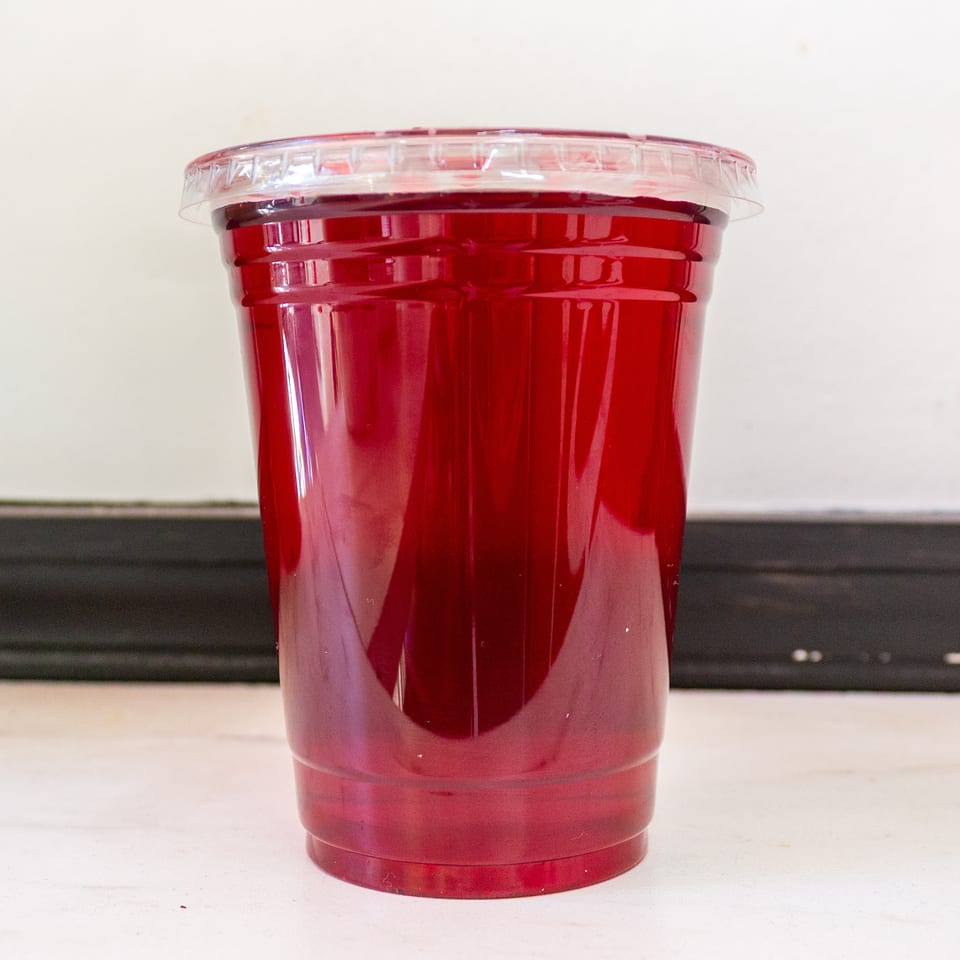 Clear plastic cup filled with a bright red beverage and sealed with a transparent lid on a countertop.