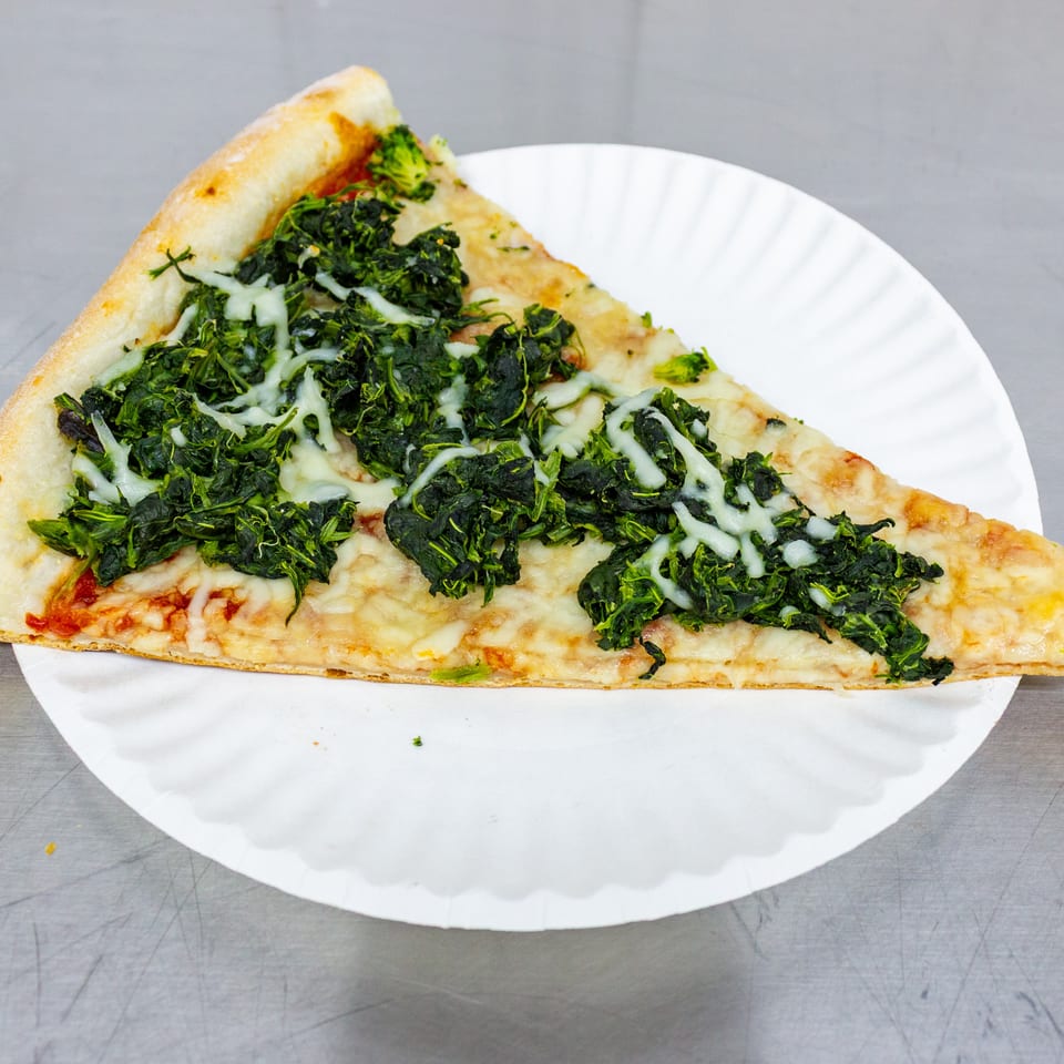 Triangular slice of cheesy spinach pizza on a white paper plate.