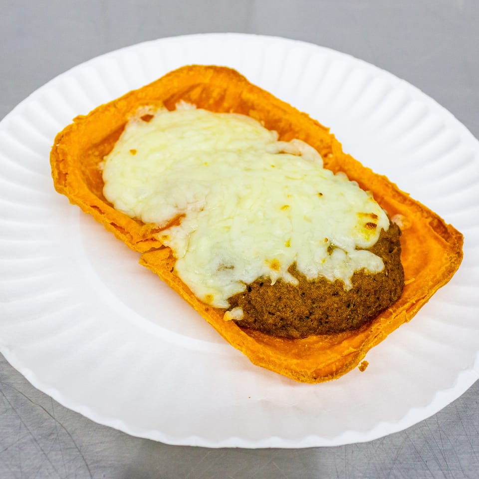Open-faced sandwich with a breaded patty, melted cheese, and tomato sauce on a white paper plate.