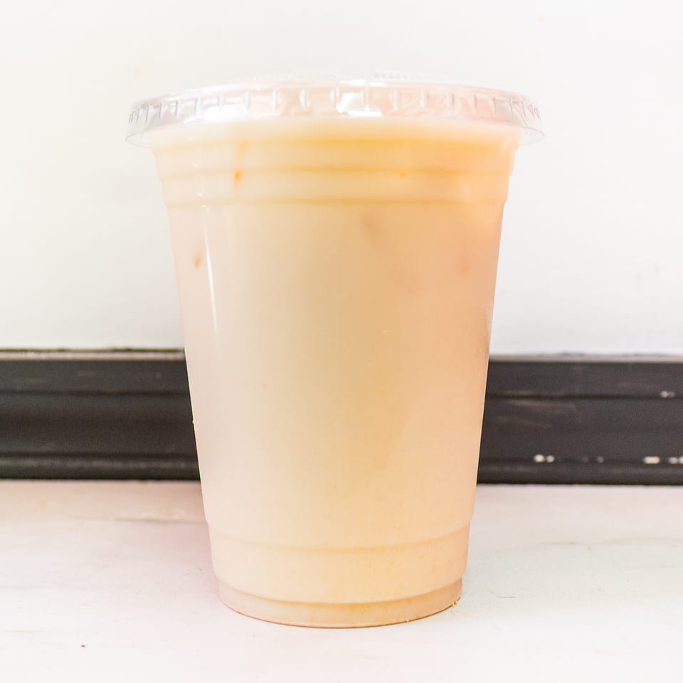 A clear plastic cup holds a pale orange creamy beverage on a white counter against a dark background.